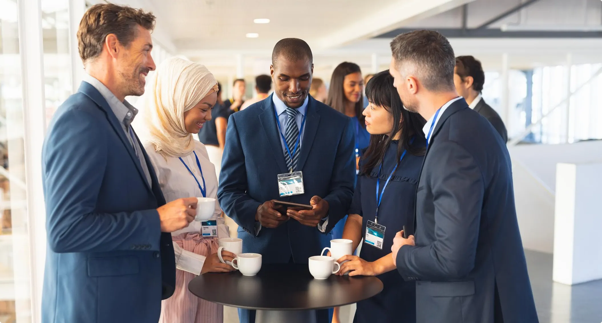 Summit guests wearing name badges talk over coffee at a standing table